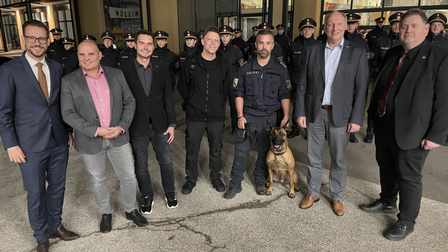 Gruppenbild von mehreren Männern vor dem MAKERSPACE Carinthia - in der Mitte sitzt ein Schäferhund der Polizei, im Hintergrund stehen Polizisten