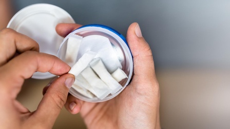 Die Hände einer Person halten eine kleine, geöffnete Dose, in der mehrere Nikotinbeutel sind