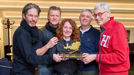 Porträt von fünf eng nebeneinander stehender Personen. Die Person in der Mitte hält eine kleine, vergoldete Statue, die die Form von Österreich hat. Davor steht Golden Ticket