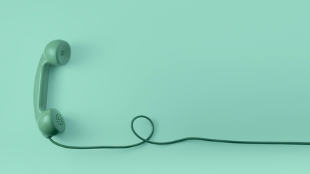 Grüner Telefonhörer mit grünem Kabel eine Schlaufe bildend vor grünem Hintergrund