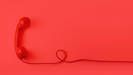 Roter Telefonhörer mit rotem Kabel eine Schlaufe bildend vor rotem Hintergrund