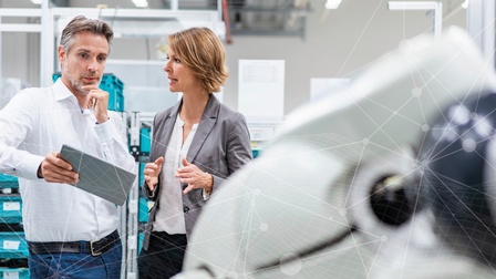 Zwei Personen mit Brillen blicken auf ein Tablet, das eine Person hält, als Overlay Schriftzug in Rot: Erfolgplus. Perspektiven denken. Erfolge lenken.