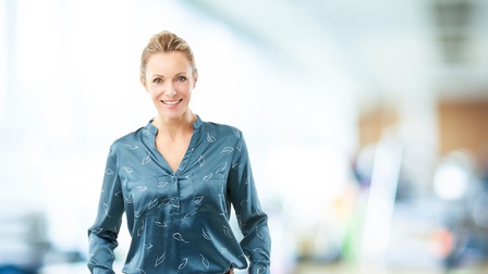 Lächelnde Person mit blauer Bluse hält Hände in Hosentaschen