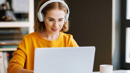 Junge Frau mit einem Gelben Pullover und Kopfhörern sitzt vor einem Laptop
