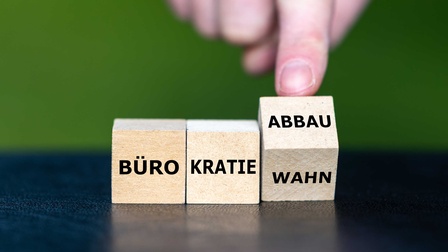 Hand dreht Würfel und ändert den Ausdruck Bürokratiewahn in Bürokratieabbau