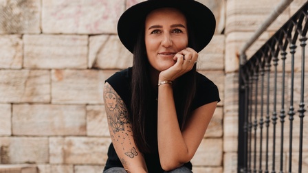 Eine junge Frau mit Hut sitzt auf Freitreppen, das Kinn in die Hand gestützt