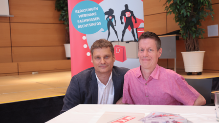 zwei Männer am Tisch vor einer Bühne