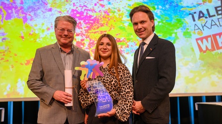 zwei Männer und eine junge Frau posieren für das Foto, sie hält einen bunten Pokal in der Hand