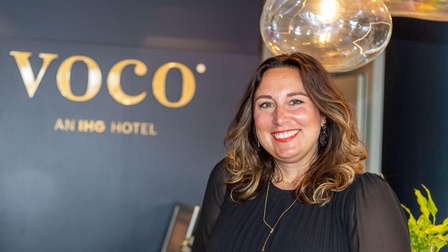 Eine lächelnde Frau vor einem Firmenlogo.