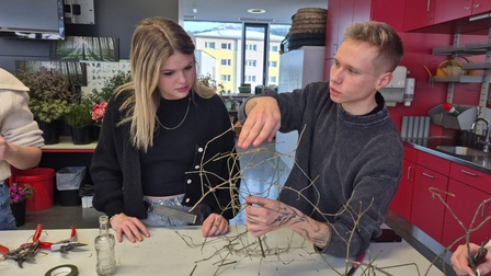 Bender und eine Schülerin hinter einem Tisch mit Waren zum Binden von Blumensträußen
