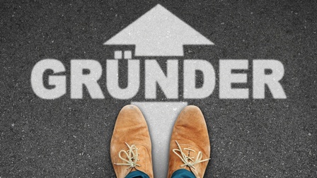 Schuhe auf Asphalt vor dem Schriftzug Gründer und einem Pfeil nach vorne