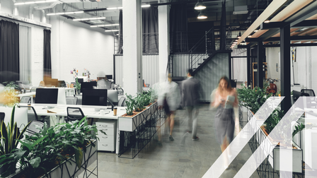 Modernes Großraumbüro mit Pflanzen und Schreibtischen, verschwommene Arbeitskollegen bewegen sich