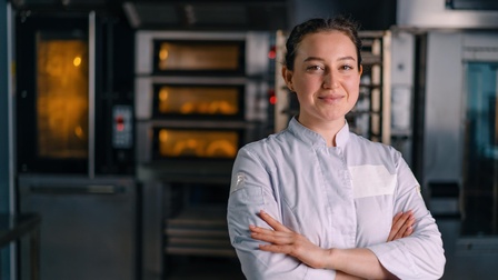 Bäckerin steht mit verschränkten Armen vor dem Backofen