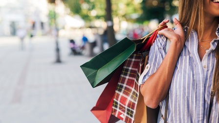 Detailansicht einer Person, die Einkaufstüten mit der Hand über die Schulter trägt