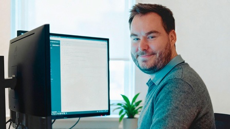 Florian Weiss sitzt am Computer und lächelt in die Kamera.