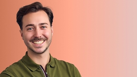 Georg Bertl lächelt in die Kamera vor orangem Hintergrund