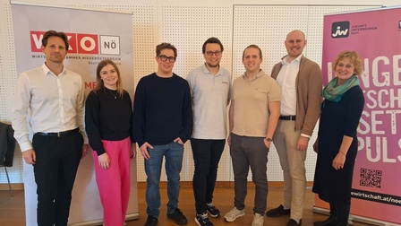 Gruppe von acht Personen steht nebeneinander in einem Veranstaltungsraum; im Hintergrund sind Roll-up-Banner der Wirtschaftskammer Niederösterreich und einer Initiative für junge Unternehmen zu sehen.