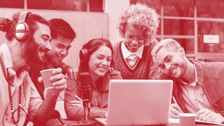 Fröhliches Team bestehend aus zwei Frauen und zwei Männern sitzt Outdoor an einem Holztisch vor einem Laptop