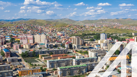 Luftaufnahme von Ulan Bator, Hauptstadt der Mongolei, im Vordergrund stehen viele mehrstöckige Wohnhäuser, im Hintergrund sieht man eine grüne Hügellandschaft.