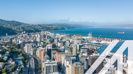 Blick auf Wellington, Neuseeland, und den Central Business District, mit vielen Wolkenkratzern, Hafen, Meer und Bergkette im Hintergrund
