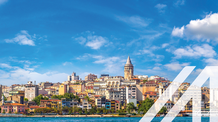 Stadtansicht von Istanbul: bunte Häuser am Wasser, in der MItte ragt der Galata Tower empor, blauer Himmel mit einigen Wolken. Über das Bild wurde ein weißes Austria A gelegt.