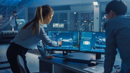 Personen in Rückenansicht in dunklem Raum mit bläulichem Licht blicken auf Monitore, auf denen Renderings von Automobilen zu sehen sind