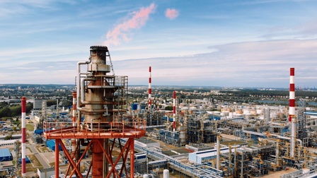 Eine große Ölraffinerieanlage. Links im Vordergrund ist ein Ölturm, aus dem Rauch aufsteigt