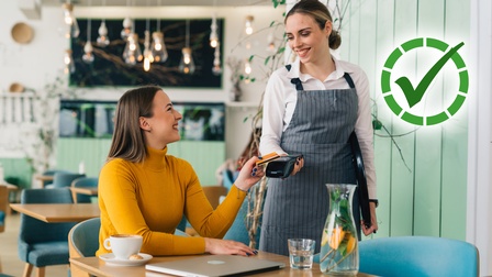 Person bezahlt im Café kontaktlos, Servicekraft hält Kartenlesegerät.