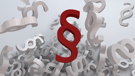 Paragrafensymbole schwirren kreuz und quer durch einen Raum. Im Vordergrund ist ein rotes Paragrafensymbol