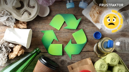 Recycling-Symbol auf einem Holztisch umringt von Müll