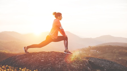 Person dehnt sich im Sonnenuntergang auf Fels stehend