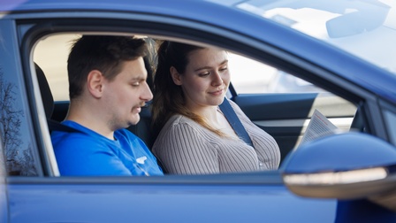 Fahrlehrer mit Fahrschülerin in einem blauen Auto