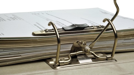 Ein Stapel Blätter in einem Ordner - der Hebelmechanismus zum Zusammenhalten der Papiere im Vordergrund