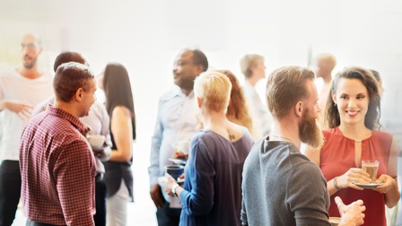 Gruppen von Personen stehen zusammen und unterhalten sich während einige von ihnen auch eine Kaffeetasse in Händen hält