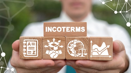 Ein im Hintergrund verschwommener Mann hält Holzwürfel. Auf einem steht Incoterms geschrieben.