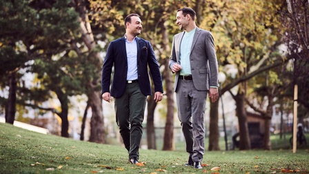 Zwei Männer spazieren redend durch eine Parklandschaft 