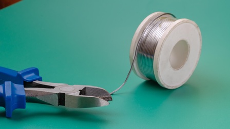 Eine Rolle Draht und links davon eine blaue Zange