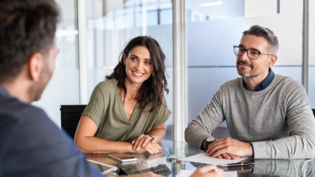 Paar im Gespräch an einem Tisch mit einem Finanzberater <br />
