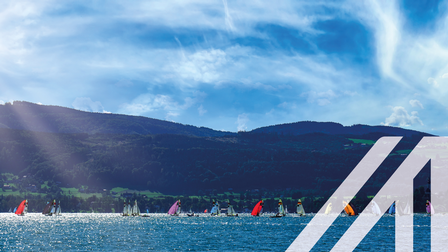 Segelboote mit bunten Segeln bei Weyregg am Attersee bei Sonnenschein unter blauem Himmel, im Hintergrund bewaldete Hügeln und Berge