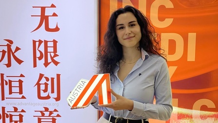 Eine junge Frau hält eine Austria-A-Zeichen in der Hand. Im Hintergrund chinesische Schriftzeichen
