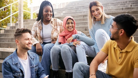 Jugendliche sitzen gemeinsam auf einer Treppe und unterhalten sich freudig miteinander