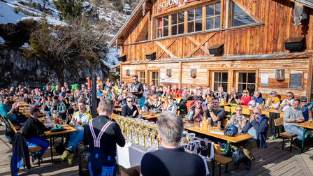 Vor einer Alm in der Sonne sitzen viele Menschen