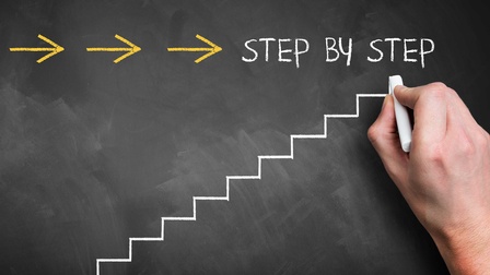 Eine Hand mit einem KReidestück schreibt auf eine Tafel 