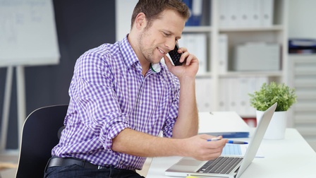 Ein freundlicher Mann im Büro am Laptop telefoniert