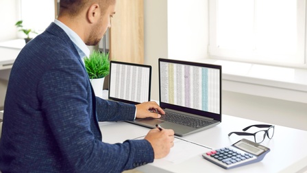 Ein Mann sitzt vor zwei Laptops - auf den Bildschirmen lange Zahlenreihen