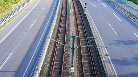 In der Mitte sind zwei Gleise parallel nebeneinander. Links und rechts von den Gleisen ist jeweils eine mehrspurige Straße