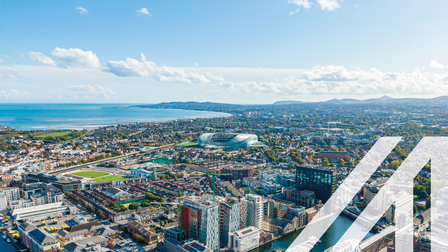 Luftaufnahme von Dublin mit Blick auf den Hafen und moderne Gebäude, im Hintergrund sieht man das Meer und Wolken am Himmel