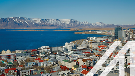 Stadtansicht von Reykjavik mit vielen roten Dächern mit modernen Hochhäusern; im Hintergrund sieht man das Meer und verschneite Berge