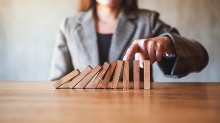 Domino Steine aus Holz fallen und werden von einer Hand einer Person in Businesskleidung aufgehalten