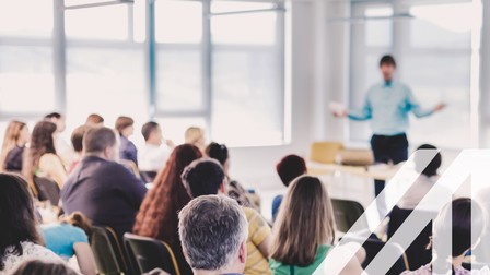 Vortragender vor einem gemischten Publikum von hinten in einem Konferenzsaal. 